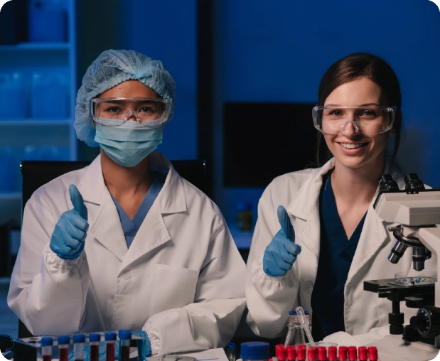 Two scientists in lab coats giving thumbs up in a laboratory.