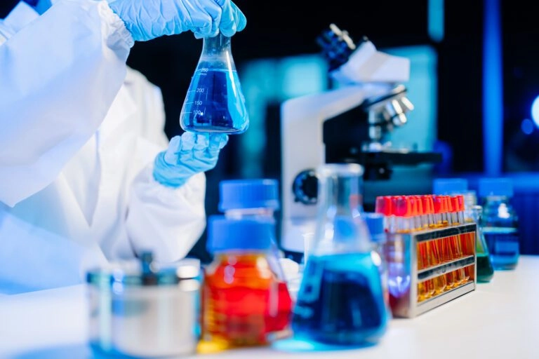 Scientist holding a blue liquid in a lab with microscopes and test tubes.